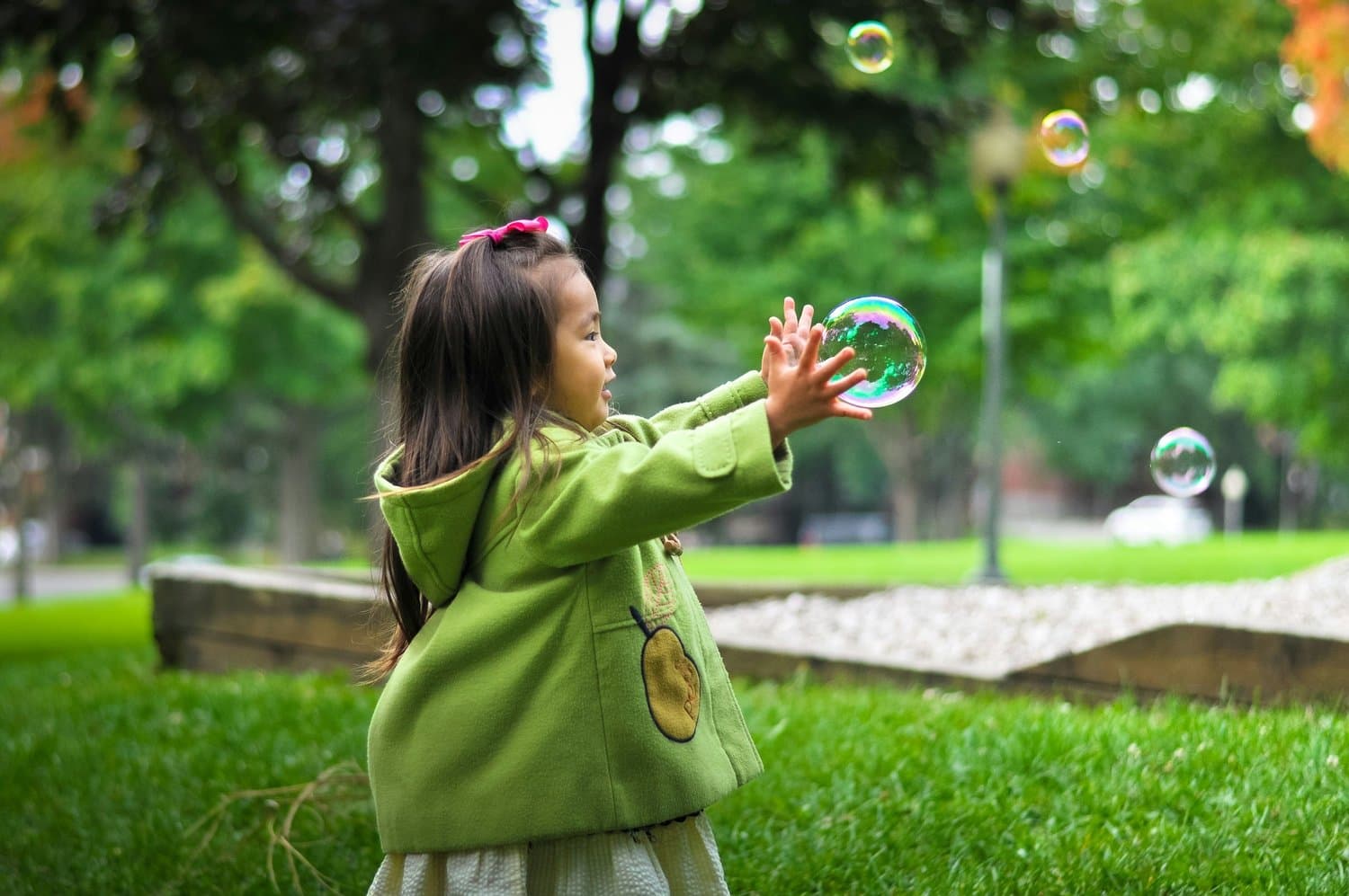 A child reaching out to a floating bubble in a green park