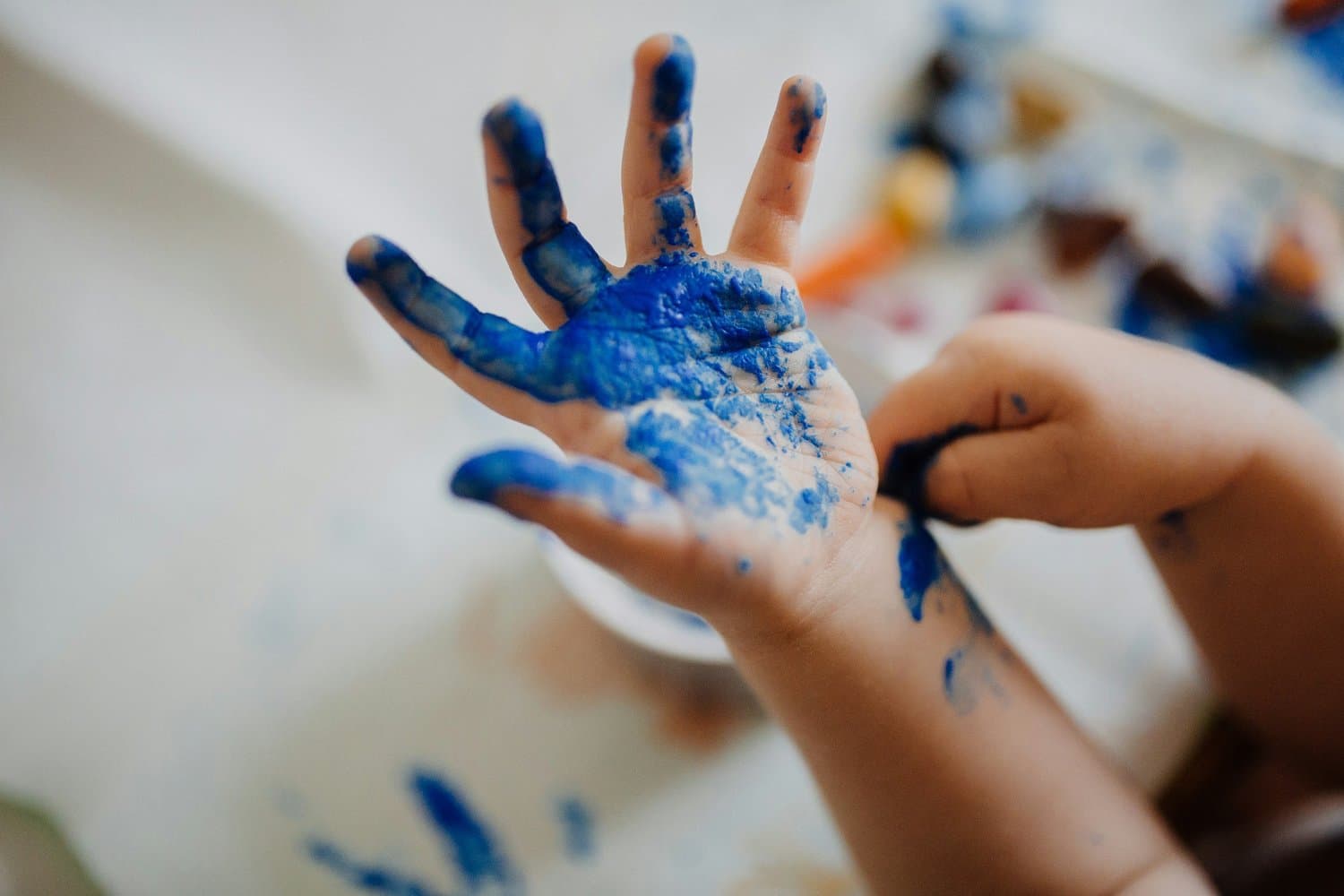 A child's hands covered in blue paint, held up to the light