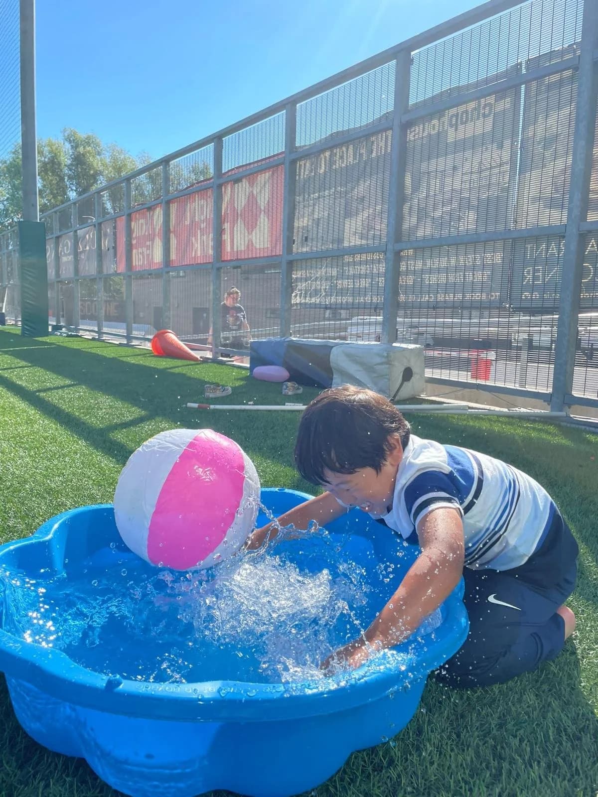 A young boy playing with a beach ball in a small pool on a sunny day