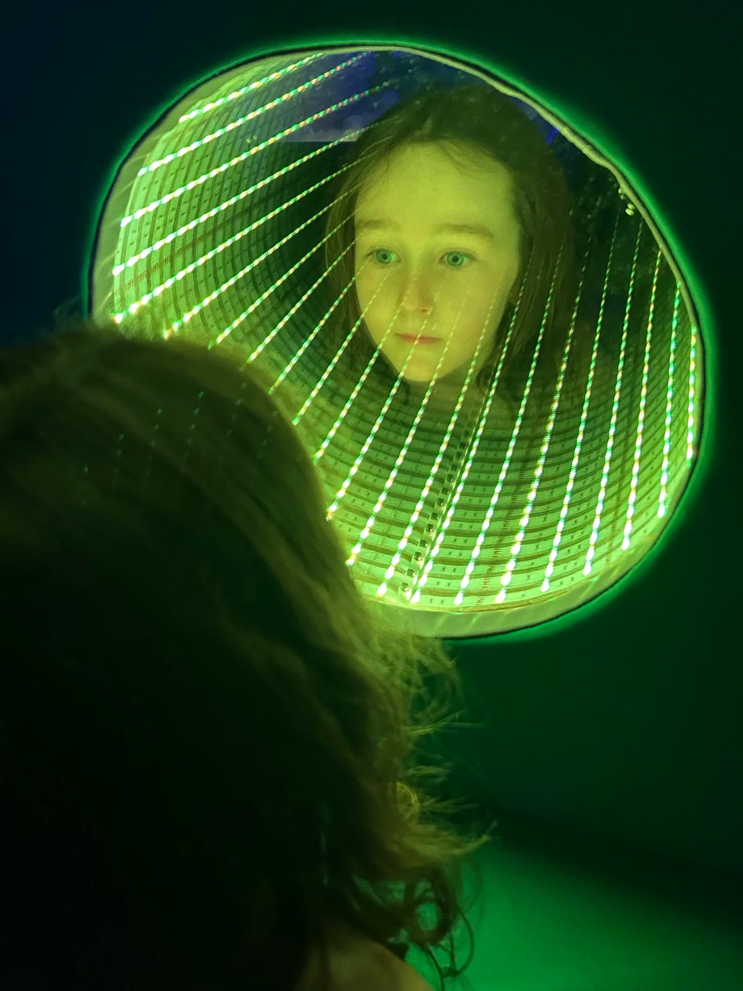 A child exploring a mirror surrounded by green LED lights in the sensory space