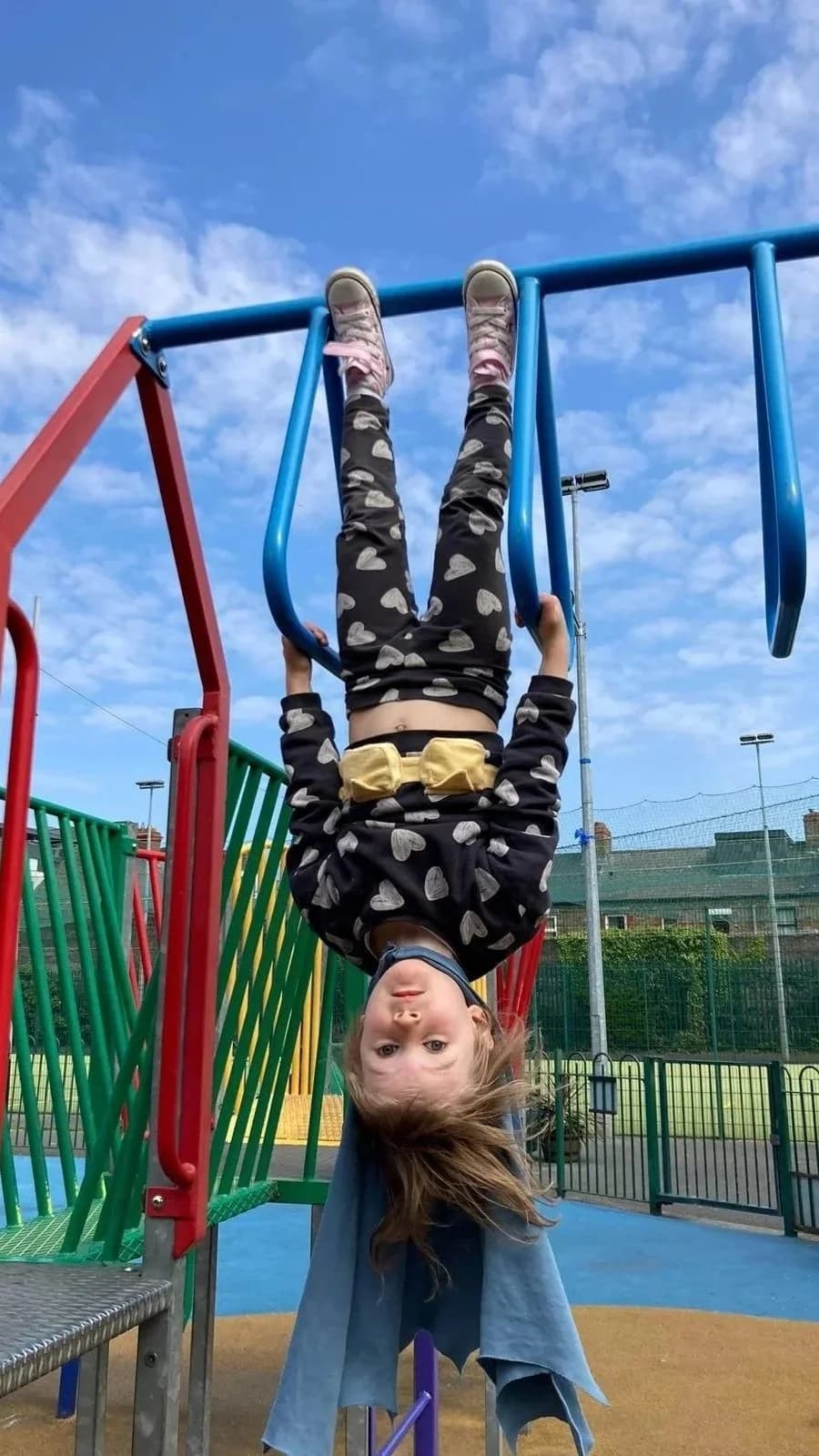 A young girl hanging upside down on playground bars against a blue sky