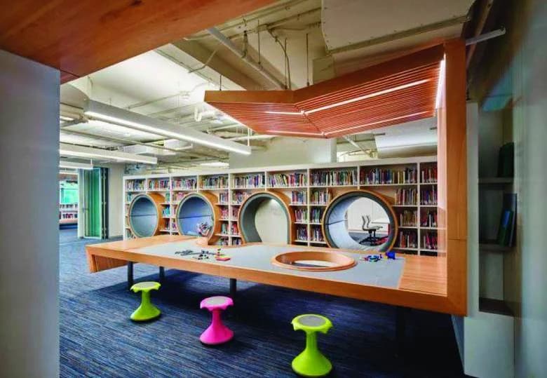 A library space with reading nooks built into round openings in the shelving, and colourful wobble stools