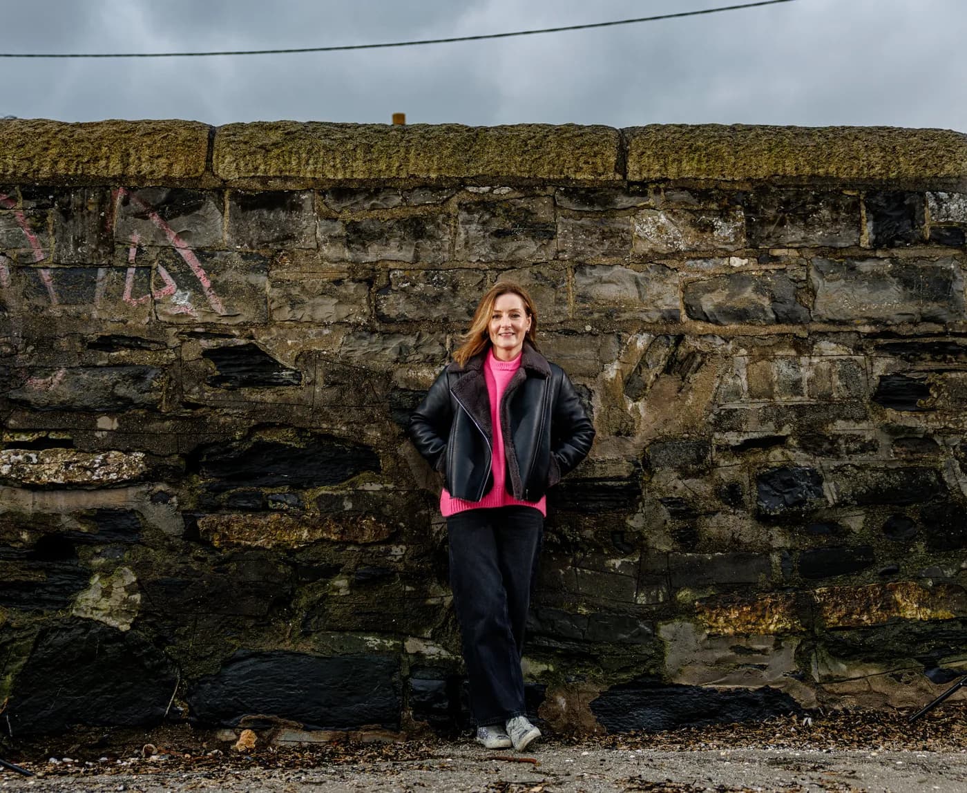 Nessa Hill, CEO of Neurodiversity Ireland, standing at a stone harbour wall under a grey sky