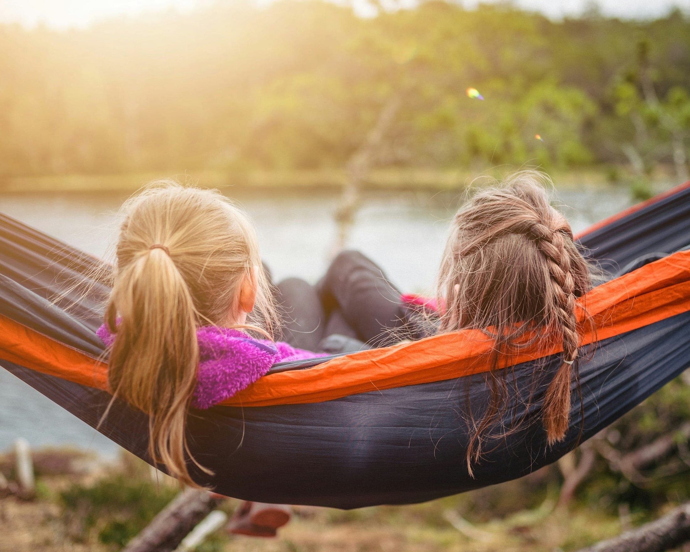 Two children lying side by side in a hammock at the edge of a lake, watching the evening light