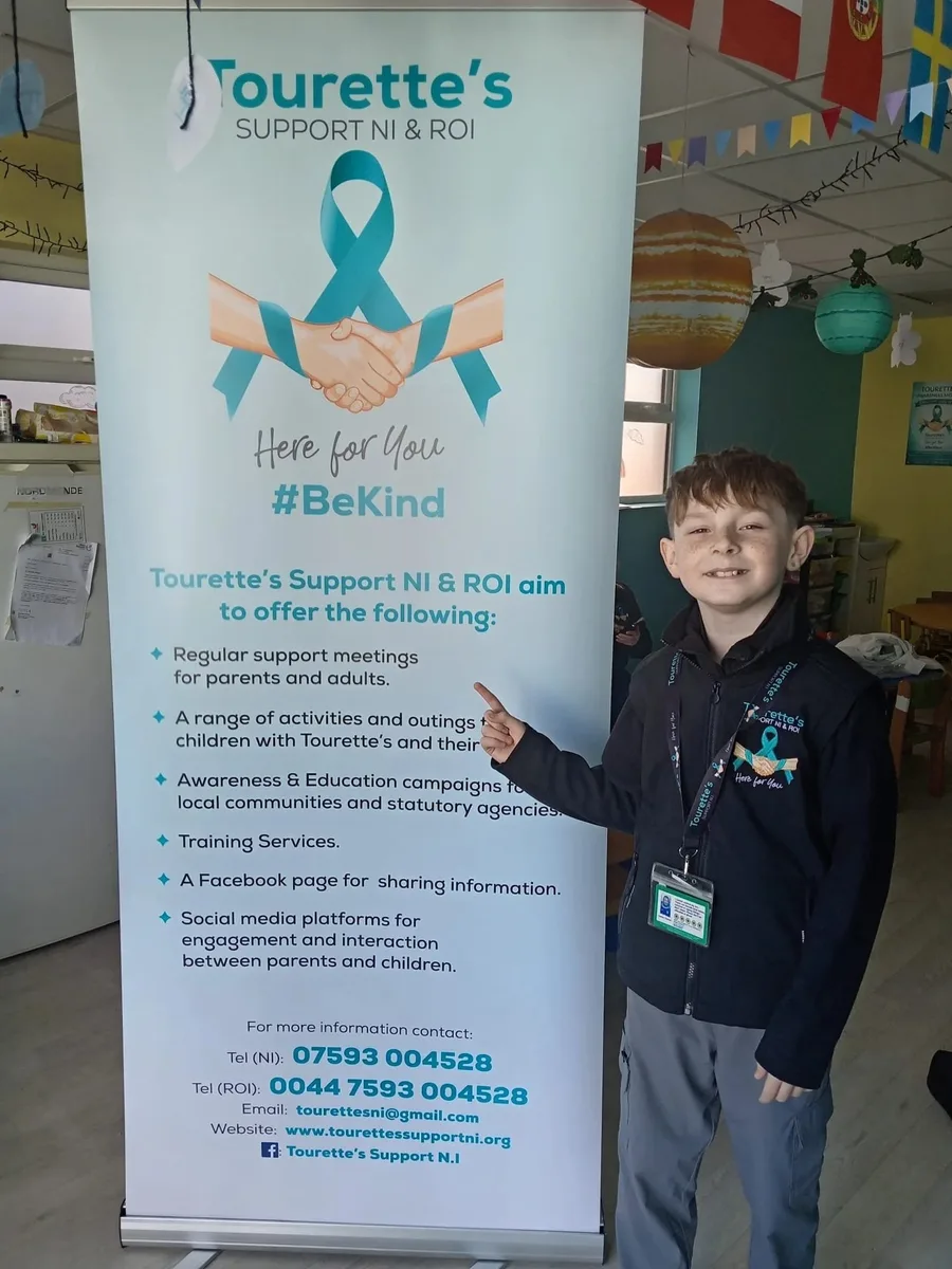 Keelan Tiernan smiling and pointing at a Tourette's Support NI and ROI banner
